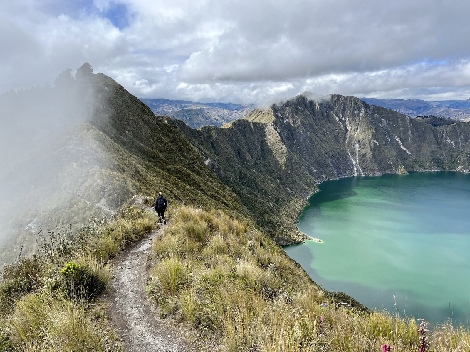 Hiker on the rim of Quilotoa crater above the turquoise lake