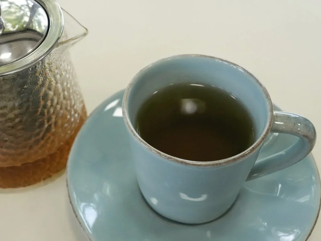 A cup of amber herbal tea on a saucer beside a glass teapot