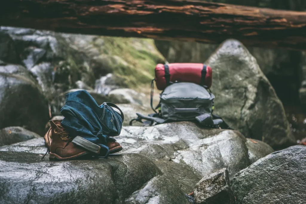 Hiking boots, a denim jacket and a backpack resting on wet rocks by a stream