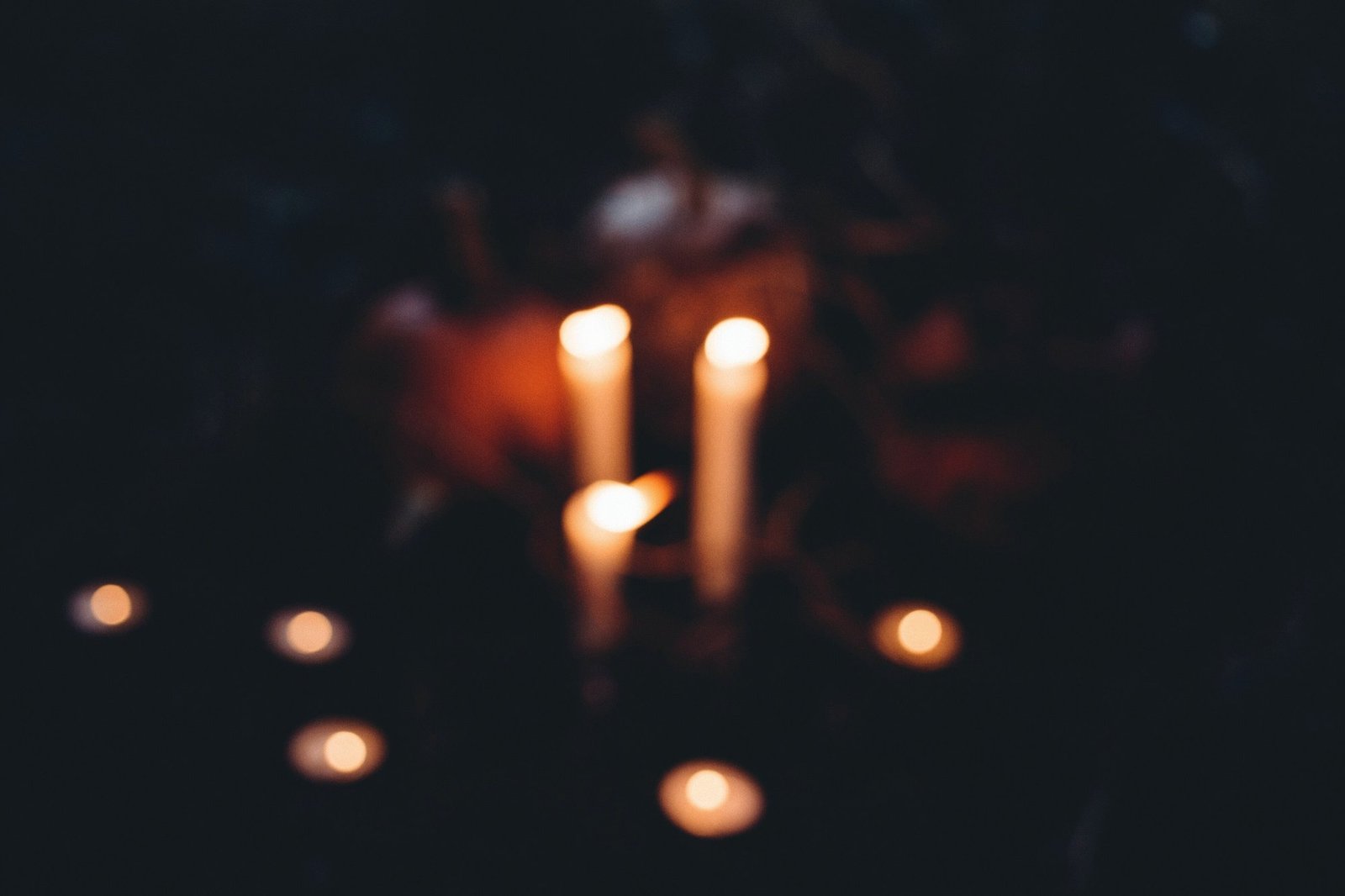 Lit candles and pumpkins, softly out of focus, on dark ground at night